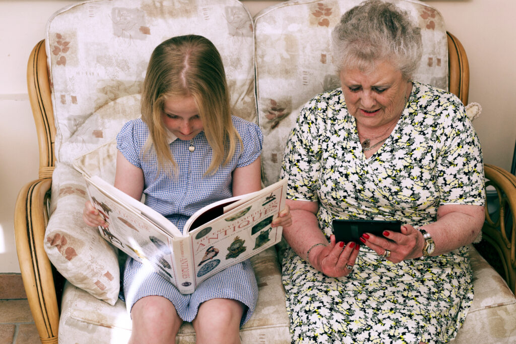An elderly lady reading an iPad and a young girl reading an antique book