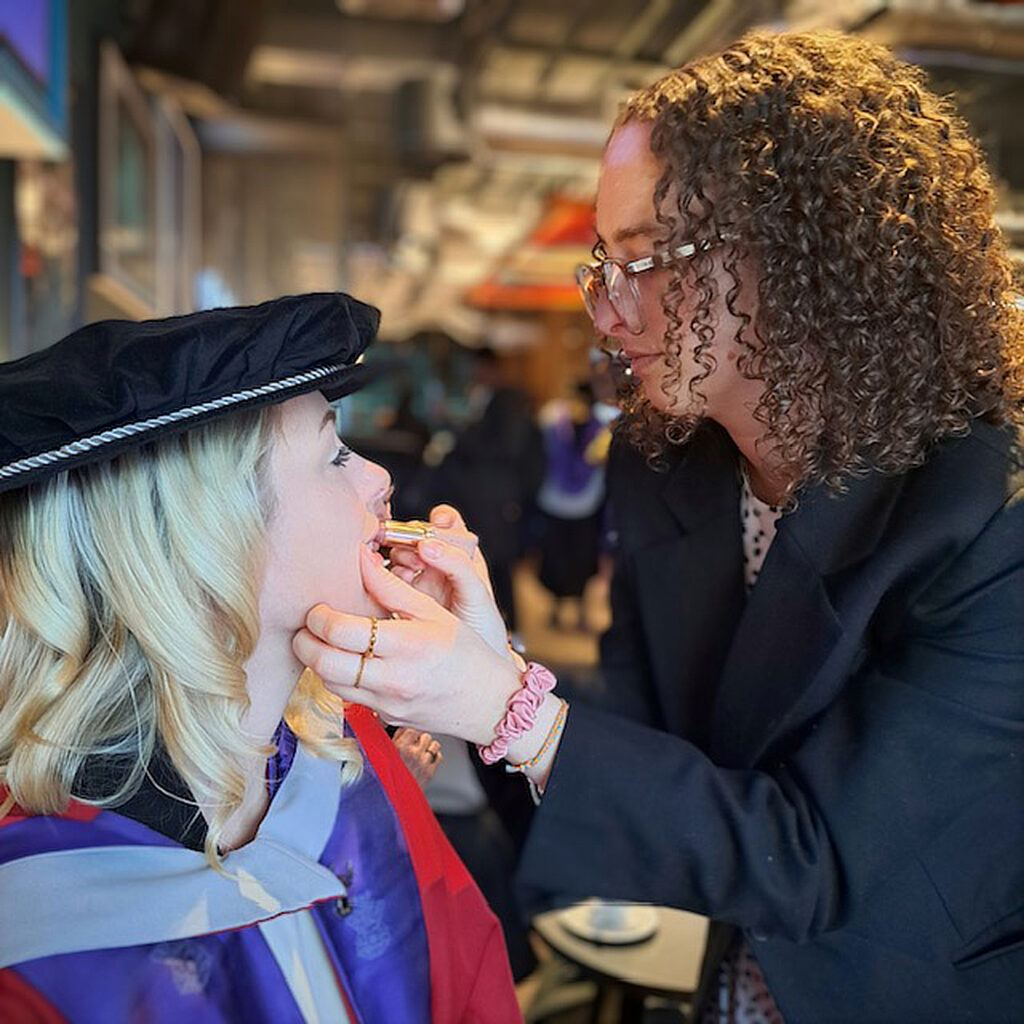 Woman applying lipstick to a girl at graduation